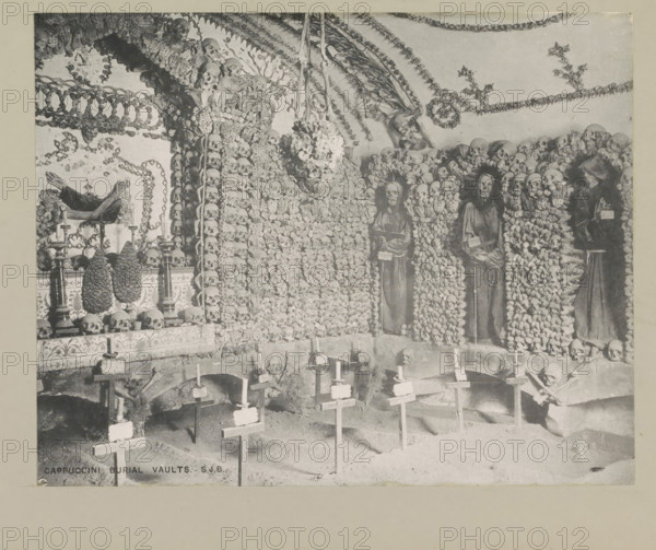 Cappuccini burial vaults, page, photomechanical print, photographer: Samuel J. Beckett, Santa Maria della Concezione dei Cappuccini, c. 1890 - c. 1900, Rome, paper, collotype, photoprint, height 151 mm x width 192 mm, charnelhouse, ossuary, A dim interior scene filled with human skulls and bones arranged into ornate patterns along the walls and arches, with rows of skulls forming columns and garlands hanging from the ceiling; three robed skeletal figures are mounted upright against the bone-covered wall, each appearing framed by surrounding skulls; a table or altar area displays skulls and candleholders, and cone-shaped objects sit on stands; in the foreground a series of simple crosses stand in the floor, each topped with a small candle, and a skeletal figure kneels near one of the crosses; chandeliers and hanging clusters of bones descend from the ceiling, and decorative motifs of bones repeat across the architectural surfaces.