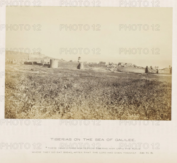 View of Tiberias in Israel, Tiberias on the sea of Galilee, photograph, page, inscription: ''There came other boats from Tiberias nigh unto the place where they did eat bread, after that the Lord had given thanks.' John VI. 23.', photographer: Francis Frith (possibly), Tiberias, c. 1850 - c. 1865, paper, albumen print, height 105 mm x width 155 mm, landscapes, tower, clock tower, monumental adornment, A wide sepia-toned landscape photograph showing a grassy foreground leading to a low stone wall and scattered buildings along a shoreline, with several rounded stone towers or fortifications rising from the wall and a few palm trees nearby, a hill with more structures visible toward the left background, and a pale sky occupying the upper portion of the image.