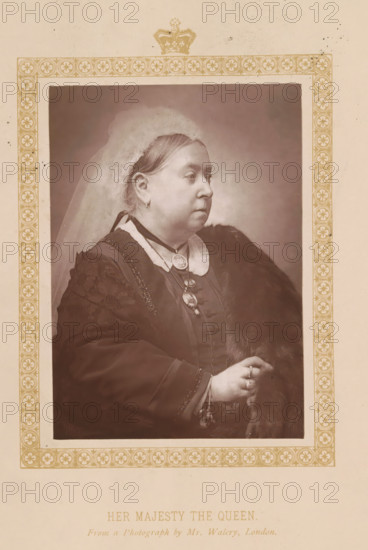 Her Majesty the Queen, page, photomechanical print, photographer: Walery, London, c. 1887 - c. 1892, printmaker, paper, Woodburytype, Woodburytypie, height 119 mm x width 85 mm, Print on frontispiece., Person, Victoria (Queen of the United Kingdom and Empress of India), veil, ruler, sovereign - BB - female ruler, A sepia-toned portrait of a woman shown in profile from the torso up, wearing a light-colored veil over her hair and a dark dress with a high collar and decorative trim, a fur draped over one shoulder, layered necklaces with medallions, earrings, and rings on her hand, set within an ornate rectangular border with repeating circular floral motifs and a crown motif at the top, all on a pale background.