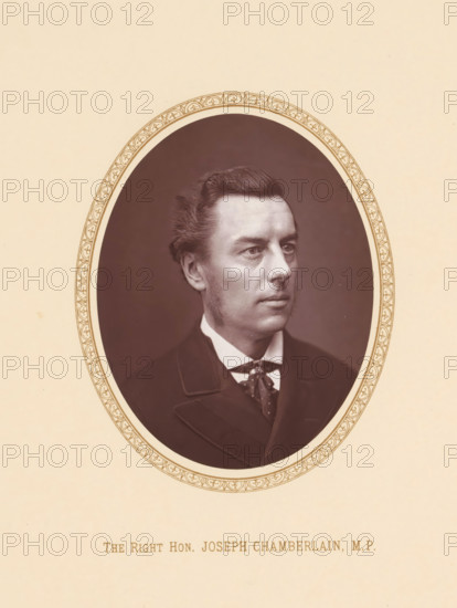 The right hon. Joseph Chamberlain, MP, page, photomechanical print, c. 1875 - c. 1880, photographer, printmaker, paper, Woodburytype, height 109 mm x width 87 mm, Person, Joseph Chamberlain, politician, eg party leader, An oval sepia portrait of a man set against a plain light background, framed by an ornate patterned border, showing his head and upper torso. He has neatly combed dark hair, sideburns, and a smooth complexion, with a neutral expression and eyes looking slightly to the side. He wears a dark formal jacket, a white shirt with a high collar, and a patterned necktie or cravat. The oval frame sits centered on a pale sheet with decorative border details and faint small spots on the background.