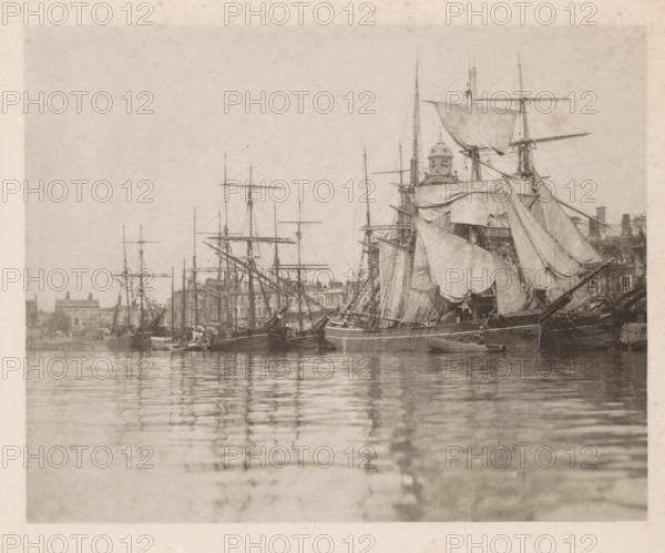 Sailing ships in the harbor of Great Yarmouth, page, photomechanical print, title: 'Great Yarmouth harbour', number: 'Plate I', photographer: Peter Henry Emerson, Great Yarmouth, cliché maker: Walter L. Colls, c. 1880 - in or before 1890, Norfolk (county), paper, photoaquatint, height 177 mm x width 221 mm, Print on frontispiece., harbour, ships (in general), A sepia-toned photograph showing a harbor scene with multiple sailing ships moored closely together, tall masts and rigging rising against a pale sky, large furled and partially unfurled sails draped across the vessels, a prominent ship in the foreground with heavy canvas and wooden hull details, smaller boats alongside, calm water in the foreground reflecting the masts and hulls, and a low line of buildings and architectural elements visible along the distant shoreline behind the ships.