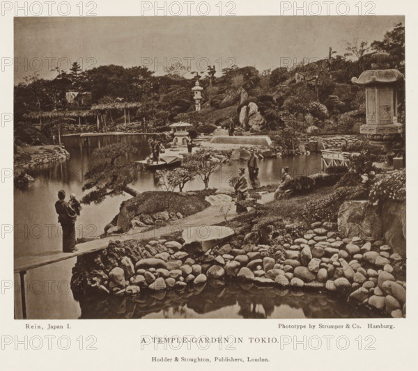 A temple-garden in Tokyo, page, photomechanical print, Tokyo, printmaker: Strumper & Co, Hamburg (city), publisher: Hodder & Stoughton, London, c. 1874 - in or before 1884, photographer, Kanto, paper, collotype, photoprint, height 115 mm x width 151 mm, garden, A sepia-toned scene showing a landscaped garden with a calm pond bordered by smooth rounded stones and irregular rocks, low manicured shrubs and small trees with twisted trunks, stone lanterns of different shapes near the water, a raised stone path and stepping stones leading across the pond, wooden bridges and simple thatched structures along the far bank, figures in traditional clothing standing or sitting near the water and on the paths, a person holding a child at the water’s edge, a large carved stone lantern with a decorative roof on the right, grassy slopes and rocky outcrops rising behind the garden, and tree-covered hills in the distant background.