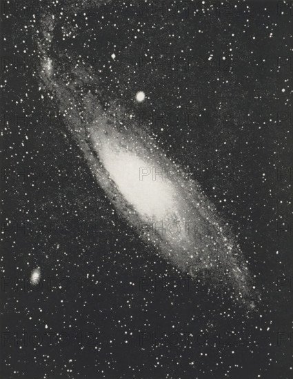 Great nebula in Andromeda, page, photomechanical print, inscription: 'Photographed by, Miss Herschel in 1783.', photographer: Isaac Roberts, 1888-12-29, printmaker, paper, autotypie, height 131 mm x width 100 mm, astronomical phenomena, A rectangular black-and-white image of a star-filled sky centered on an elongated, bright nebulous shape with a dense bright core and a tapered outer region, surrounded by numerous small bright points on a dark background and a few slightly larger circular bright spots.