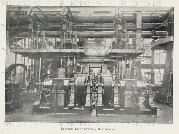 Electric light stations, Manchester, page, photomechanical print, photographer: Brothers, WJ, c. 1889 - in or before 1899, printmaker, paper, autotypie, height 109 mm x width 157 mm, power station, exterior, representation of a building, A wide interior view of an industrial room filled with large metal machinery and piping, showing multiple heavy cylindrical flywheels and curved belts in the foreground mounted on sturdy bases, a raised platform with railings and vertical supports running across the midsection, complex networks of pipes and fittings overhead and behind the platform, structural columns and beams framing the space, various valves, gears, and smaller mechanical components scattered around the floor level, and tall windows at the rear letting in light.