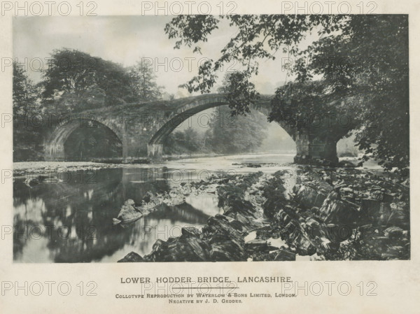 Lower Hodder Bridge, Lancashire, page, photomechanical print, photographer: JD Geddes, printmaker: Waterlow & Sons Limited, c. 1889 - in or before 1899, paper, collotype, photoprint, height 101 mm x width 161 mm, landscape with bridge, viaduct or aqueduct, A monochrome scene showing a stone arched bridge spanning a calm river, with two large arches visible and a rocky riverbank in the foreground; overhanging tree branches frame the top and right edges, while dense trees and foliage fill the background on both sides of the bridge and reflect faintly in the water below.