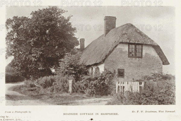 Roadside cottage in Hampshire, page, photomechanical print, photographer: FW Brookman, West Norwood, printmaker: Meisenbach's Autotype Company, c. 1889 - in or before 1899, FW Brookman, Meisenbach's Autotype Company, London, paper, autotype, half-tone engraving, height 92 mm x width 156 mm, cottage, façade (of house or building), A small thatched cottage with textured walls sits beside a winding dirt road, a window with divided panes visible on the upper wall and a smaller window lower down, a brick chimney rises from the roof, and a wooden picket gate stands near overgrown shrubbery and plants in front of the building; a large leafy tree towers to the left, casting shadows over the cottage and surrounding grassy verge under a pale sky.