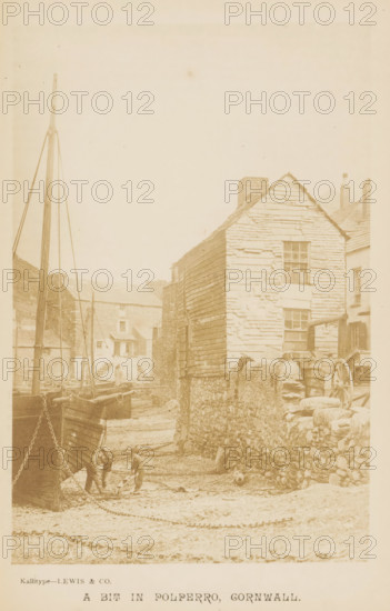 Ship on the street in Polperro, A bit in Polerro, Cornwall, photograph, page, photographer: Lewis & Co., J., Polperro, c. 1881 - in or before 1891, paper, callitype, height 142 mm x width 94 mm, street, building a ship, ship under construction, A faded photograph showing a narrow quay with wooden boats beached on a muddy shore and tall masts rising beside them, a stone wall running along the right side topped by a low parapet, an old timber-clad building with visible weathered planks and multiple windows standing above the wall, a wooden wheel and stacked barrels near the building, a row of distant stone and plaster buildings beyond the boats, and two small figures on the shore near the foreground interacting with a small boat.