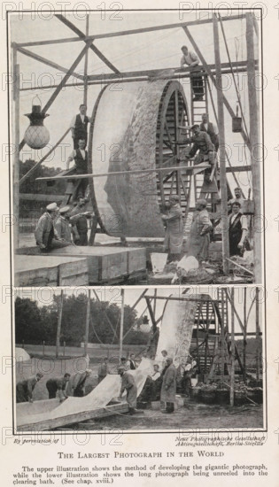 Developing and washing a large panoramic photograph on a roll, The largest photograph in the world, page, photomechanical print, inscription: 'The upper illustration shows the method of developing the gigantic photograph, while the lower illustration shows the long photograph being unreeled into the clearing bath. (See chap. xviii.)', photographer: Neue Photographische Gesellschaft, c. 1898 - in or before 1908, printmaker, paper, autotype, height 192 mm x width 120 mm, Prints opposite title page., photographic apparatus, A tall wooden frame supports a large cylindrical drum with a textured surface being worked on by several men; some men stand on ladders and platforms around the drum while others stand or kneel on the ground nearby, and a few men wear aprons or coats. A hanging lamp with a patterned globe is suspended from the frame on one side. Wooden beams, ropes, and pulley elements are visible around the structure. In the lower portion a long sheet is being unrolled or handled by a...