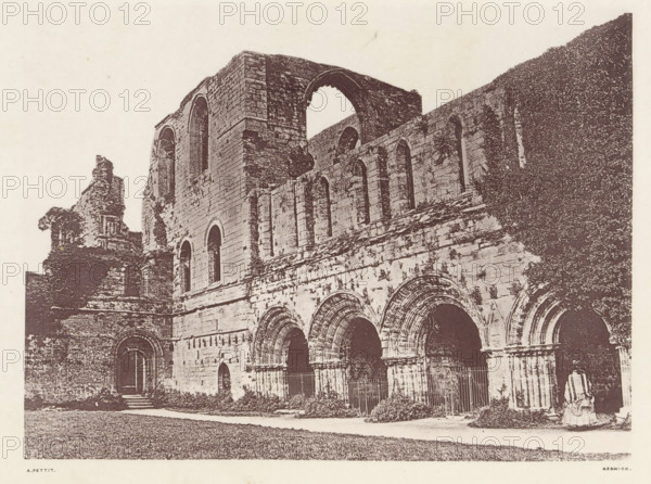 View of the courtyard of the ruins of Furness Abbey, Furness Abbey_the cloisters court, page, photomechanical print, photographer: Alfred Pettitt, Furness Abbey, Keswick, c. 1870 - in or before 1880, paper, heliotype, height 127 mm x width 172 mm, courtyard, abbey, monastery, convent, Roman Catholic church, Cumbria, A sepia-toned photograph shows a large stone building with a series of arches and tall narrow windows, some arches forming doorways and others set higher in the wall; the masonry appears weathered and textured, with sections of ruined upper walls and an opening where a large arch is partially intact; vegetation climbs part of the facade and low shrubs grow at the base, while a paved path runs along the front and an expanse of grass is visible in the foreground; a fragment of a statue or carved figure sits near one corner of the building.