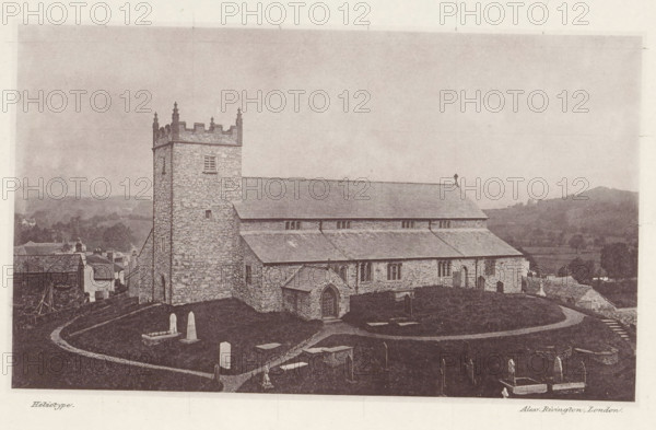 View of Saint Michael and All Angels Church in Hawkshead, Hawkshead church, page, photomechanical print, photographer: Alex Rivington, Hawkshead, London, c. 1870 - in or before 1880, paper, heliotype, height 107 mm x width 181 mm, church (exterior), Cumbria, Saint Michael and All Angels Church, A stone church with a square tower and crenellated top stands on a grassy hill, its long pitched roof and stone walls visible along with a small arched porch entrance and several narrow windows. A curving path winds through a churchyard containing various headstones and tombs of different shapes and sizes, some enclosed by low railings. In the background there are rolling hills and scattered trees, and adjacent to the church a cluster of small buildings and rooftops can be seen. The image has a sepia tone and an overall aged photographic appearance.
