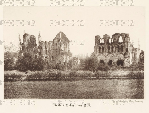 Wenlock Abbey from NW, View of the ruins of Wenlock Priory, page, photomechanical print, photographer: J. Laing, Wenlock Priory, cliché maker: anonymous, c. 1867 - in or before 1877, Shropshire, Much Wenlock, paper, collotype, photoprint, height 125 mm x width 189 mm, ruin of church, monastery, A wide sepia-toned image showing the ruins of a large stone abbey set behind a low wall and a strip of grass in the foreground, with two main ruined sections separated by vegetation; the left section features tall arched windows, partial walls, and a gabled roofline with surrounding trees and shrubs, while the right section shows a façade with large arched openings and upper window arches, all set against a pale sky.