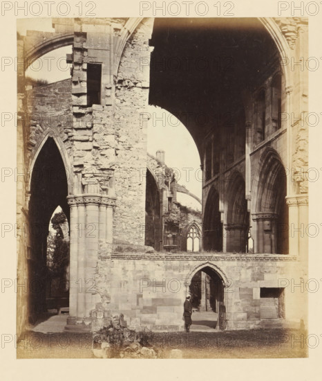 Interior of the ruins of Melrose Abbey with a man at a doorway, photograph, page, number: '(No. 8.)', title: 'Interior', inscription: 'Exhibiting Organ Screen with fine Chain of Leaves on Moulding. The Nave broken by a modern wall to support the building. To the left, the narrow North Aisle, with exquisitely-carved foliage on Capitals of Pillars.', photographer: WJ Pringle, Melrose Abbey, c. 1860 - in or before 1870, Melrose (Scotland), paper, albumen print, height 165 mm x width 141 mm, interior of church, ruin of church, monastery, A sepia-toned photograph shows a large stone ruin with tall arched openings and columns, rough textured masonry, and decorative capitals on some columns; one man in period clothing stands near a smaller arched doorway in the lower right, looking toward the interior; through the arches other remnants of stone walls, window openings with pointed tops, and sweeping vaults are visible, along with scattered rubble and low vegetation on the ground.