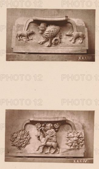 Two woodcarvings in Worcester Cathedral, page, photomechanical print, Above a basilisk between (presumably) two wolves, below a man on a goat between two stylized leaf motifs., number: 'XXXIII, XXXIV', c. 1863 - in or before 1873, paper, Woodburytype, Woodburytypie, height 306 mm x width 244 mm, interior of church, goat, carving, applied arts, basilisk (cock with posterior of snake), A photograph shows two horizontal carved wooden panels mounted one above the other on a pale background, each panel featuring sculpted reliefs within rectangular frames topped by curved caps. The upper panel displays a central griffin-like creature with a scaled body and feathered wings, flanked by two smaller four-legged animals facing inward; the wood shows carved texture and worn surfaces. The lower panel depicts a human figure seated on a stag or similar hoofed animal, holding a curved object, with stylized floral or foliate clusters carved on either side; the figure's garment has a diamond pattern and...