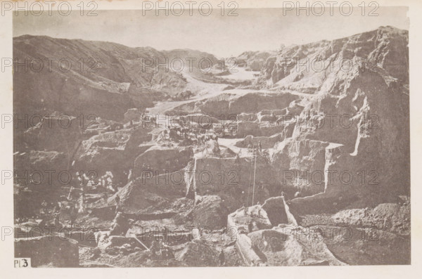 View of a diamond mine in South Africa, presumably near Kimberley, page, photomechanical print, number: 'Pl. 3', photographer: Gray Brothers (possibly), South Africa, c. 1870 - in or before 1880, paper, collotype, photogravure, height 125 mm x width 192 mm, Print in rear image section., mine, Kimberley, A monochrome image showing a rugged, terraced rocky landscape with steep cliffs and carved steps. The scene features a series of ledges and platforms cut into the rock, with visible tool marks and exposed strata. Small groups of figures stand and work on various levels, some near simple wooden frameworks and carts, and a few animals are present on the higher terraces. Narrow paths and ramps connect the different levels, and ropes or lines hang down one section of the rock face. The sky above is pale and unobstructed, and the image has a textured, aged appearance.