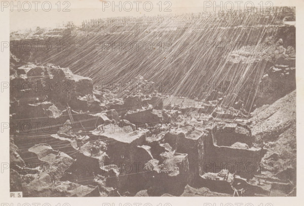 View of the diamond mine at Kimberley in South Africa, page, photomechanical print, number: 'Pl. 5', photographer: Gray Brothers, Kimberley, c. 1870 - in or before 1880, paper, collotype, photogravure, height 126 mm x width 189 mm, Print in rear image section., mine, A sepia-toned photograph of a rocky landscape with steep, jagged cliffs and scattered large boulders, over which numerous thin, bright diagonal lines run from the upper right toward the lower left, creating a streaked pattern across the image; the foreground shows irregular rock surfaces and crevices with lighter patches on some edges, a slender ladder leaning against a rock, and several taut lines stretched horizontally and diagonally among the stones, while the upper edge of the scene reveals a rough rim of rock and a faint horizon.