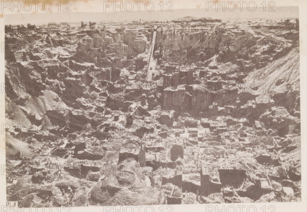 View of a diamond mine in South Africa, presumably near Kimberley, page, photomechanical print, number: 'Pl. 8', photographer: Gray Brothers (possibly), South Africa, c. 1870 - in or before 1880, paper, collotype, photogravure, height 127 mm x width 190 mm, Print in rear image section., mine, Kimberley, A high-contrast monochrome aerial view of a large excavation site showing steep terraced rock faces and irregular square and rectangular cutouts, with exposed strata creating a stepped pattern across the scene and narrow ledges and pathways between the cut blocks, scattered equipment and small structures visible on some ledges, a long straight ramp or track running from the upper edge toward the center, a few small vertical poles and thin cables spanning parts of the pit, rough rubble and loose rock piles at various levels, and a narrow strip of lighter sky and distant low land along the top edge.
