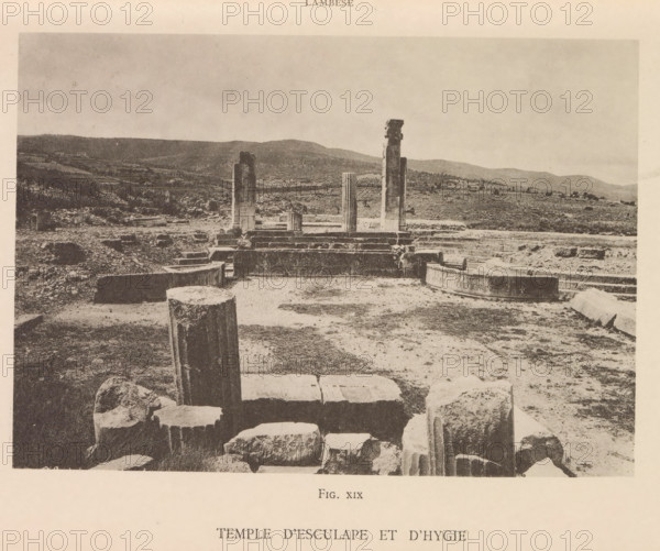 Temple d'Esculape et d'Hygie, View of the ruins of a temple of Asclepius and Hygieia at Lambaesis in Algeria, page, photomechanical print, number: 'Fig. XIX', Algeria, maker: Berthaud Frères, France, c. 1884 - in or before 1894, photographer, North Africa, paper, collotype, photoprint, height 106 mm x width 150 mm, ruin of a building, architecture, Lambaesis, A wide sepia photograph shows an archaeological site with scattered stone blocks and columns in various states of ruin across a dirt and grassy terrain, a few standing column fragments rising from a stepped platform in the midground, rounded and fluted column sections and irregular rock fragments in the foreground, low rolling hills and sparse vegetation in the background, and an expansive sky above.