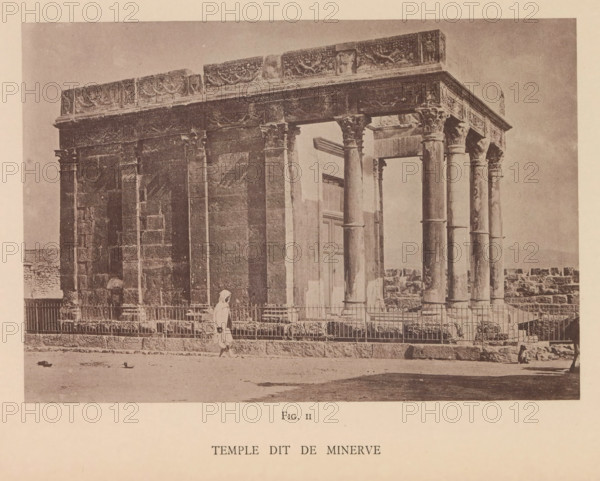 Temple dit de Minerve, View of the de Minerva temple in Tébessa, page, photomechanical print, number: 'Fig. II', Tébessa, maker: Berthaud Frères, France, c. 1884 - in or before 1894, photographer, North Africa, paper, collotype, photoprint, height 107 mm x width 157 mm, temple, shrine, Roman religion, A sepia-toned photograph of an ancient stone building with a colonnaded facade showing decorative friezes along the top and carved capitals on the columns, a gated low fence in front of the structure, an arched doorway set back between columns, a person wearing a light-colored cloak walking along the front of the fence, scattered stones and small debris on the ground in the foreground, and a low stone wall extending from the right side of the building.