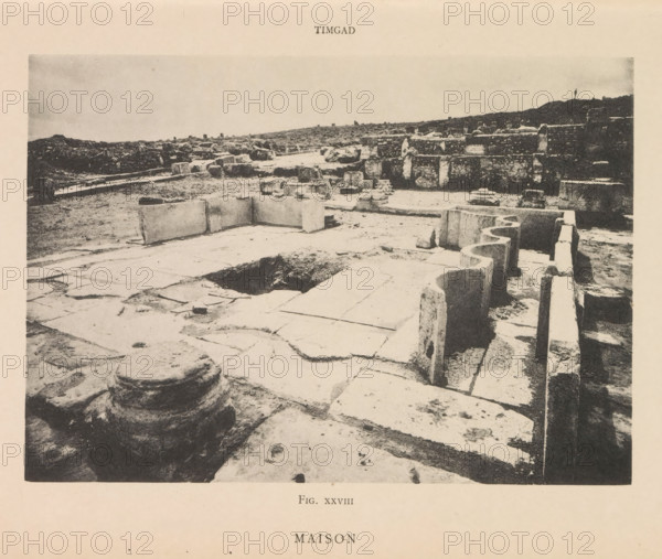 View of the Roman ruins of a house in Timgad, Maison, page, photomechanical print, number: 'Fig. XXVIII', Timgad, maker: Berthaud Frères, France, c. 1884 - in or before 1894, photographer, North Africa, paper, collotype, photoprint, height 111 mm x width 157 mm, ruin of a dwelling, house, castle, A wide, sepia-toned photograph of an archaeological ruin showing large stone slabs and blocks arranged on a flat ground, with carved stone edges and rounded stone features in the foreground. The scene includes a rectangular depression in the paved surface and several upright and fallen stone blocks scattered across the area. Along the right side there is a low stone wall with curved cutouts and a narrow trench beside it. In the background are low mounds of earth and additional ruined stone structures stretching to the horizon under a pale sky.