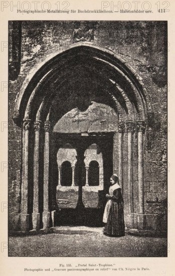 Portal Saint-Trophime, Woman in front of a portal of the Cathédrale Saint-Trophime in Arles, page, photomechanical print, number: 'Fig. 135.', photographer: Charles Nègre, Arles, cliché maker: anonymous, c. 1900 - in or before 1905, Provence-Alpes-Côte d'Azur, paper, autotypie, height 171 mm x width 114 mm, adult woman, parts of church exterior and annexes: portal, Saint-Trophime (Arles), A grainy black and white image showing a large stone arched portal with multiple rounded arch layers and paired columns on each side, a dark interior beyond the arch with two smaller arched openings visible in silhouette, a woman in period dress and a head covering standing near one of the columns on the right side, textured stone walls surrounding the doorway, and a flat stone floor in the foreground.