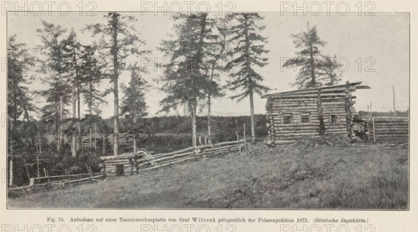 Exterior of a hunting hut in Siberia, Sibirische Jägerhütte, page, photomechanical print, inscription: 'Aufnahme, 1872.', number: 'Fig. 76.', photographer: Wilczek, Siberia, cliché maker: anonymous, c. 1900 - in or before 1905, paper, autotype, height 89 mm x width 179 mm, log-cabin, A wide landscape in muted tones shows a grassy foreground leading up to a rustic log building with visible horizontal logs and small square window openings, flanked by a low log fence that curves toward a cluster of tall, thin trees with sparse foliage; additional logs and stacked wood appear near the building, and a distant tree line stretches across the horizon under a pale sky.