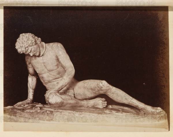 Sculpture The Dying Gaul in the Capitoline Museums, photograph, page, Rome, c. 1850 - in or before 1860, photographer, paper, albumen print, height 97 mm x width 130 mm, piece of sculpture, reproduction of a piece of sculpture, Capitoline Museums, A monochrome photograph of a reclining male marble statue set against a dark background, showing the statue's torso, head tilted downward, curly hair, one arm supporting the body with a hand on the base, and legs extended with visible muscle and anatomical detail; the statue rests on a textured rectangular plinth with visible edges and surface wear, and the image has a pale border around the dark central area.