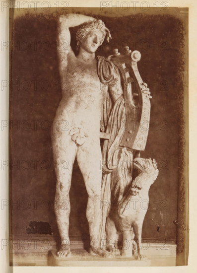 Apollo citharaedus in the Capitoline Museums, photograph, page, Rome, c. 1850 - in or before 1860, photographer, paper, albumen print, height 141 mm x width 97 mm, Photo after page 16., piece of sculpture, reproduction of a piece of sculpture, (story of) Apollo (Phoebus), Capitoline Museums, A sepia-toned photograph shows a classical marble statue of a nude male figure standing on a rectangular base, one arm raised to touch his head and the other resting on a large lyre beside him draped with cloth. The statue displays a leaf covering at the groin and detailed hair and facial features, with a muscular torso and legs. At the lyre's side, a sculpted animal with a long neck and open mouth rises upward, its front paws on the base near the figure's feet. The background is dark and textured, and the image has a light border around the edges.