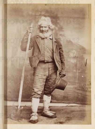 Portrait of an unknown man with a shovel and a hat in his hand, photograph, page, Rome, c. 1850 - in or before 1860, photographer, paper, albumen print, height 134 mm x width 97 mm, historical persons not known by name, adult man, A full-length portrait of an older man standing and facing forward, wearing a worn jacket over a buttoned shirt and patched trousers tucked into wrapped leggings, with a thick white beard and tousled hair; he holds a long wooden staff upright in one hand and a top hat by its brim in the other, with scuffed shoes visible at his feet against a plain backdrop.