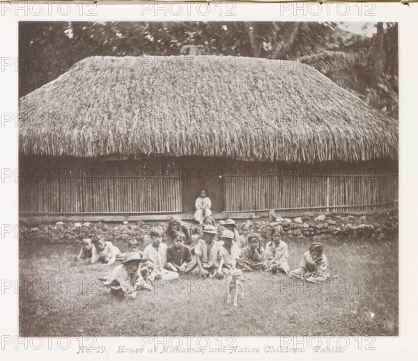 House at Mahaena, and Native Children.Tahiti, House in Mahaena with children from Tahiti in front of it, page, photomechanical print, number: 'No. 19.', photographer: Henry Stuart-Wortley, Tahiti, cliché maker: Meisenbach's Autotype Company, printer (person): Meisenbach's Autotype Company, 1880, Meisenbach's Autotype Company, photographer, French Polynesia, paper, collotype, photoprint, height 138 mm x width 166 mm, housing, child (at home), A large thatched roof hut fills the upper portion of the image with dense, straw-like material hanging over a structure of vertical wooden slats and a raised stone foundation, a narrow doorway at the center where a seated figure is visible, and in front of the building a group of people sit and recline on grass, some wearing wide-brimmed hats and loose clothing, with a small dog standing on the grass closer to the camera.
