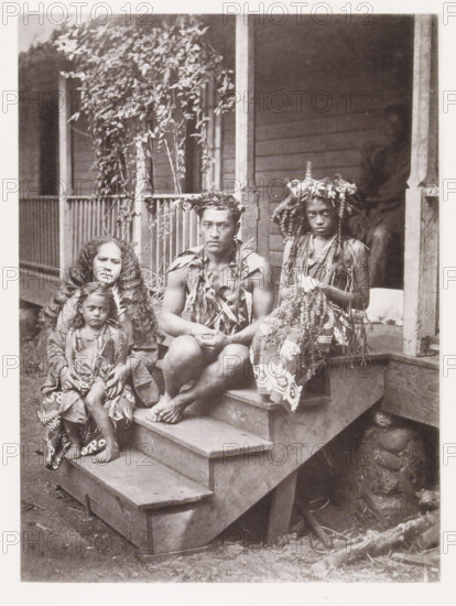 Portrait of a family from Tahiti, sitting on a step in front of the house where they work as servants, Our family of Servants at Tahiti, page, photomechanical print, number: 'No. 8.', photographer: Henry Stuart-Wortley, Tahiti, clichémaker: Meisenbach's Autotype Company, printer (person): Meisenbach's Autotype Company, 1880, Meisenbach's Autotype Company, photographer, French Polynesia, paper, collotype, photogravure, height 168 mm x width 125 mm, house personnel, servants, A sepia photograph shows four people seated on wooden steps in front of a porch with vertical posts and leafy vines climbing beside them. A man sits near the center wearing a crown of leaves and a garment made of foliage draped over his shoulders, his hands resting in his lap and his legs bare. A woman to his left has long loose hair and holds a small child on her lap; the child has a wrapped garment and bare feet. To the man’s right a young person wears a headdress of flowers and foliage and a patterned skirt, with...