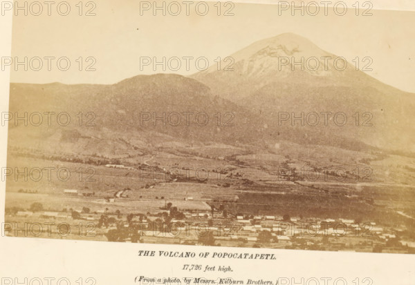 The volcano of Popocatapetl, photograph, page, inscription: '17, 726 feet high.', photographer: Kilburn, Mexico, c. 1870 - in or before 1880, North America, paper, albumen print, height 90 mm x width 154 mm, volcano, Popocatépetl, A sepia-toned photograph showing a broad landscape with a large snow-capped mountain rising behind a lower rounded hill, a patchwork of lighter and darker fields spreading across the midground, and a row of small rectangular buildings along the bottom edge, with a pale sky above.