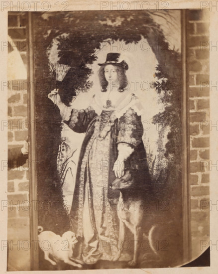 Photo reproduction of a painting, depicting a portrait of Leonora Christina Ulfeldt, photograph, reproduction, page, photographer: Julius Wulff, after painting by Karel van Mander (I), c. 1858 - in or before 1862, paper, albumen print, height 235 mm x width 183 mm, female royal bastard, A sepia-toned framed portrait shows a person in ornate historical clothing standing within a painted arch of foliage, wearing a dark brimmed hat with curled hair visible at the sides and a lace-trimmed collar and sleeves; one hand holds a fan while the other rests on the head of a large dog beside them, and a smaller dog sits near the hem of the long patterned gown.