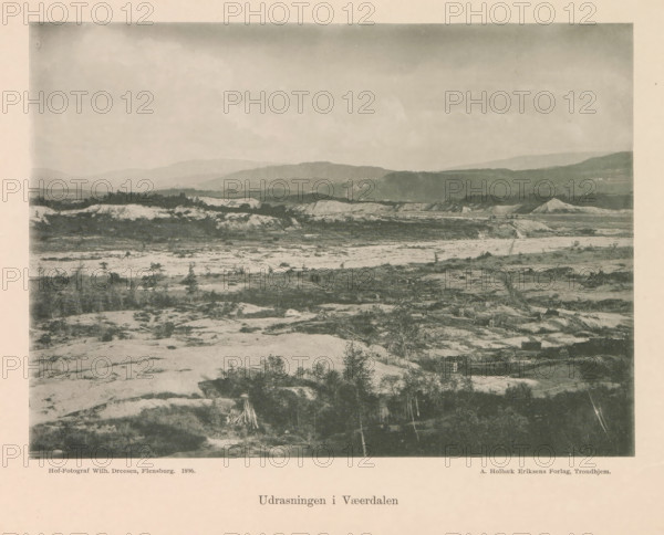 View of excavations or soil purification at probably Verdal, Udrasningen i Vaeerdalen, page, photomechanical print, maker: Wilhelm Dreesen, Verdal, publisher: Holbæk-Eriksen, A., Trondheim, c. 1896 - in or before 1897, paper, collotype, photoprint, height 159 mm x width 221 mm, mountains, digging (industrial process), A wide sepia-toned landscape photograph showing a rocky foreground with sparse low vegetation and scattered small trees, a middle ground of rough terrain with exposed pale earth and darker patches of shrubs and brush, and a background of layered hills and ridges fading into the distance under a cloudy sky.
