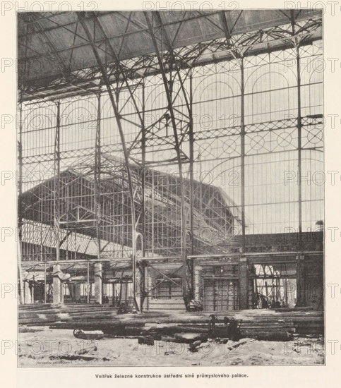 Construction of the Industrial Palace under construction in Prague, Stavba veze na prumyslovem paláci dne 15. ledna r. 1891, page, photomechanical print, Výstavište, cliché maker: Carl Bellmann, Prague, 1891-01-15, photographer, paper, autotypie, height 218 mm x width 190 mm, building-site, A large interior space dominated by tall iron framework and arched glass panels fills the scene, with slender vertical columns and intersecting diagonal supports forming a lattice against the translucent wall panels; elaborate iron trusses and curved braces span the upper area, and a pitched roof structure with additional metal scaffolding and beams is visible behind the foreground framework. The lower foreground shows a rough floor surface scattered with long cylindrical logs and beams lying parallel, and a few pieces of machinery or carts near the piled timbers. Throughout the image there are layered metal walkways, platforms, and open archways with visible vertical and horizontal bars, and the ov...