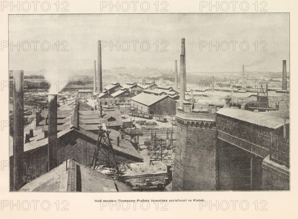 Hute soustavy Thomasovy Prazské zelezárské spolecnosti na Kladne, Exterior of an ironworks in Kladno, page, photomechanical print, Kladno, cliché maker: Carl Bellmann, Prague, c. 1890 - in or before 1895, photographer, Bohemia, paper, autotypie, height 170 mm x width 262 mm, exterior of industrial structures, factories, A wide industrial scene with numerous brick buildings and long sloping roofs, tall cylindrical smokestacks rising from various points, and one stack emitting a plume of white smoke; metal frameworks, pipes, and scaffolding are visible among rooftop machinery and equipment; a large ornate brick structure with patterned masonry and an attached metal lattice walkway appears in the foreground on the right; rows of smaller gabled factory buildings extend toward the middle ground, interspersed with additional chimneys and open yards containing scattered materials and railway cars; the distant background shows a hazy flat landscape and low-lying structures under a pale sky.