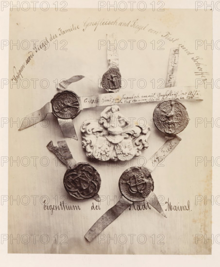 Family coat of arms and seal of the Gensfleisch family and seals of the Fust and Schöffer families, photograph, page, number: '30', photographer: B. Erdmann, Mainz, c. 1867 - in or before 1872, Rhineland-Palatinate, paper, albumen print, albumendruk, height 197 mm x width 164 mm, armorial bearing, heraldry, seal, stamp, A sepia-toned photograph shows several round wax seals attached to narrow strips of paper arranged around an ornate carved crest. The crest is sculpted with flowing scrollwork and a central raised figure. The seals vary in design and texture, some showing raised emblems or figures and others with complex patterned borders; each is affixed to a frayed paper tail. The seals and crest are displayed against a plain light background with visible faint stains and slight discoloration near the edges. There is decorative cursive writing along the top and bottom margins of the image.