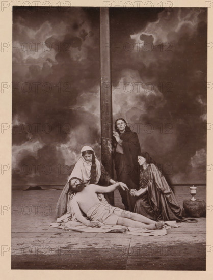 Pietà, page, photomechanical print, photographer: Carl Stockmann, Oberammergau, cliché maker: anonymous, c. 1885 - in or before 1890, Bavaria, paper, collotype, photoprint, height 224 mm x width 166 mm, 'Pietà ', 'Vesperbild', 'Marienklage' (no others present): Christ, either with or without crown of thorns, mourned by Mary, group of actors, troupe, actors on the stage, A sepia-toned staged scene showing a horizontal wooden beam or crosspiece rising from the floor toward the top, set against a cloudy backdrop. A shirtless man lies on the floor draped with a cloth, his head tilted back and eyes closed, with a beard and long hair. A woman wearing a light-colored head covering and cloak kneels behind him, supporting his head and looking downward. Another woman in darker drapery kneels at his side, holding his hand and gazing toward him. A standing figure in a dark cloak leans against the vertical beam, hands clasped and looking upward. A small covered vessel sits on a rounded stone to the...