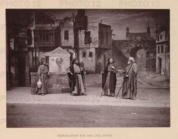 Preparations for the last supper, page, photomechanical print, inscription: 'Gemeinde Oberammergau Passionsspiel 1890', photographer: Carl Stockmann, Oberammergau, cliché maker: anonymous, c. 1885 - in or before 1890, Bavaria, paper, collotype, photoprint, height 168 mm x width 227 mm, group of actors, troupe, actors on the stage, the episode of the Last Supper, A staged scene shows four figures in long robes standing on a wooden floor in front of a painted backdrop of an old stone street with buildings and an arched gateway; two of the figures hold long staffs, one holds a jug, and another rests a hand on a stone fountain structure that has a carved face relief; the figures wear head coverings or cloaks and have varied facial hair and hairstyles, while the backdrop depicts textured walls, shuttered windows, and architectural details such as balconies and stone steps under a cloudy sky.