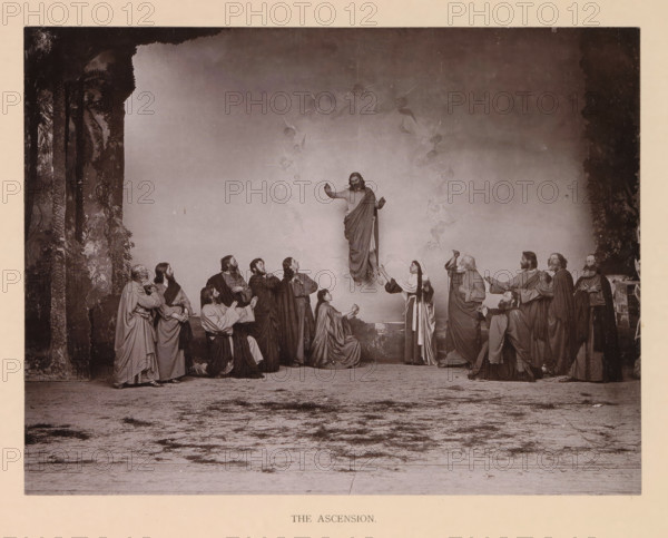 The ascension, page, photomechanical print, inscription: 'Gemeinde Oberammergau Passionsspiel 1890', photographer: Carl Stockmann, Oberammergau, cliché maker: anonymous, c. 1885 - in or before 1890, Bavaria, paper, collotype, photoprint, height 176 mm x width 230 mm, Print after page 132., group of actors, troupe, actors on the stage, Christ aloft in the sky, Ascension, A sepia-toned scene shows a robed figure elevated above a group, with arms raised and draped cloth flowing around the body, surrounded by faint winged figures forming a vertical arc; below, a circle of men and women in long robes stand, kneel, or reach upward with varied gestures and facial expressions, some looking up and some holding hands, arranged across a stage-like ground with a textured foreground; tall dark foliage frames the left and right edges of the scene, creating a backdrop against a plain wall behind the central figures.