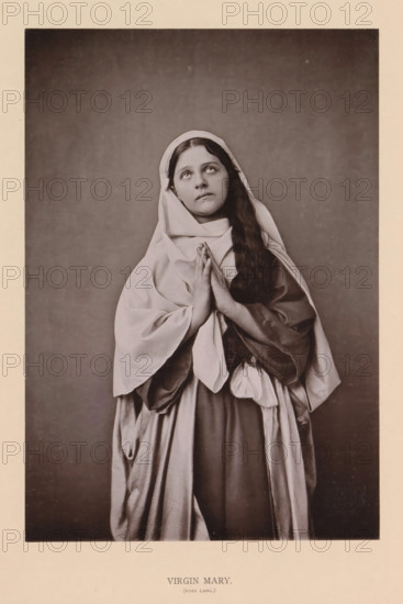 Virgin Mary (Rosa Lang), page, photomechanical print, inscription: 'Gemeinde Oberammergau Passionsspiel 1890', photographer: Carl Stockmann, Oberammergau, cliché maker: anonymous, c. 1885 - in or before 1890, Bavaria, paper, collotype, photoprint, height 215 mm x width 150 mm, Person, Rosa Lang, portrait of actor, actress, the Virgin Mary, A sepia-toned portrait of a young woman standing against a plain dark backdrop, wearing layered draped garments and a head covering, with long hair falling over one shoulder, hands held together in front of her chest, eyes looking upward, and a calm facial expression.