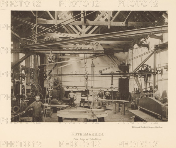 Interior with employees of the boiler shop of the machine factory of Gebroeders Stork & Co, Boiler Shop. Punching, Cutting and Planing Room, page, photomechanical print, number: 'No. 11.', Hengelo (Overijssel), maker: Emrik & Binger, Haarlem, c. 1884 - in or before 1894, photographer, paper, collotype, light print, height 155 mm x width 217 mm, factory-building, factory-interior, machine shop, A sepia-toned photograph shows an industrial interior with exposed wooden roof beams and a network of overhead metal rails, pulleys, chains, and beams. Large machinery, gears, and hanging hooks occupy the space, with round metal plates and cylindrical supports on the floor. Several men in work clothing stand or sit among the equipment, one man positioned at the front near a large circular workpiece and others grouped further back. The walls are plain and show shafts and mounted wheels, and various rods and belts run across the scene connecting machines. The image has a pale border surrounding the...