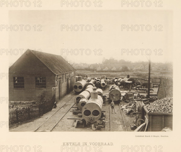 Boilers in stock, View of steam boilers at the machine factory of Stork & Co. Brothers, page, photomechanical print, number: 'No. 14.', Hengelo (Overijssel), maker: Emrik & Binger, Haarlem, c. 1884 - in or before 1894, photographer, paper, collotype, photogravure, height 156 mm x width 211 mm, factory-building, steampower (alleg.) (technical aspects, crafts, industries, agriculture), A sepia-toned scene shows an industrial yard with long cylindrical metal boilers and pipes arranged on parallel tracks, many displaying riveted circular ends, surrounded by scattered metal parts and stacks of materials; a wooden building with a pitched roof and multi-pane windows stands to the left, a narrow fenced path runs alongside it, and a man in work clothes and a hat walks between the tracks near the foreground; in the middle distance there are low houses and trees forming a horizon, and a tall pole rises near the right side of the yard.