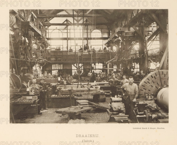 Turning shop. (South side), Interior with employees of the machine factory of Gebroeders Stork & Co, page, photomechanical print, number: 'No. 8.', Hengelo (Overijssel), maker: Emrik & Binger, Haarlem, c. 1884 - in or before 1894, photographer, paper, collotype, photogravure, height 154 mm x width 214 mm, factory-building, factory-interior, machine shop, A large industrial interior with high windows and exposed beams fills the scene, showing numerous metal machines, gears, chains, pulleys, and workbenches arranged across the floor and along raised platforms; a group of men in work clothes stand and sit among the equipment, some near a large circular gear-like wheel on the right and others by heavy blocks and machine parts in the center and left; hanging chains descend from the ceiling and scaffold-like wooden and metal structures frame the space, while scattered tools, stacked plates, and mechanical components lie on tables and the floor, and a balcony with railings runs across the bac...