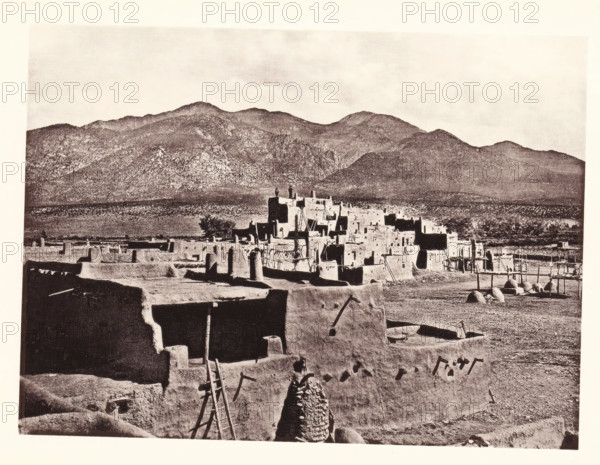 North Pueblo of Taas, page, photomechanical print, number: 'Fig. 27.', photographer: John Karl Hillers, United States of America, cliché maker: Heliotype Printing Company, Boston (Massachusetts), c. 1876 - in or before 1881, North America, Massachusetts, paper, collotype, photoprint, height 161 mm x width 218 mm, city-view in general, 'veduta', mountains, façade (of house or building), A sepia-toned scene shows a cluster of multi-level adobe buildings with flat roofs, protruding wooden beams, ladders leaning against walls, and rounded door and window openings; a foreground adobe wall with a rough opening and a leaning ladder frames the view, and a conical stone or adobe structure stands near the wall; beyond the main cluster are more adobe structures, fenced enclosures, and dome-shaped oven-like forms on the ground; a wide plain separates the settlement from a backdrop of rugged, tree-covered mountains under a pale sky.