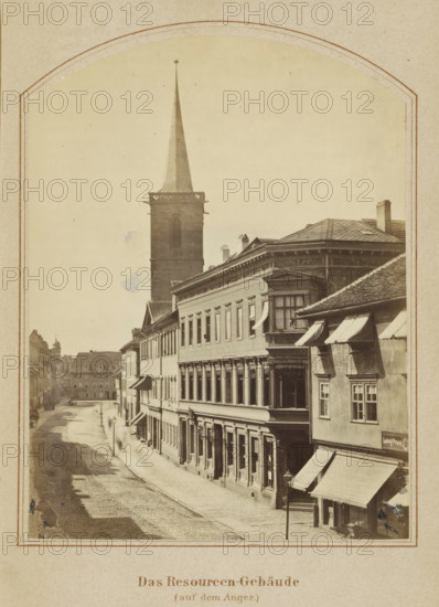 Das Resourcen-Gebäude (auf dem Anger), View of buildings along the Anger in Erfurt, photograph, page, number: '7', Erfurt (city), c. 1858 - in or before 1868, photographer, Thuringia, paper, albumen print, height 131 mm x width 99 mm, Image opposite page 88., street, square, circus, façade (of house or building), A sepia-toned street scene framed by a rounded arch shows a row of multi-story buildings lining a cobbled road, with a tall church tower and spire rising behind the structures. The foremost building on the right has a decorative cornice, a bay window, and awnings over ground-floor windows and entrances, while the adjacent façades display regularly spaced windows and ornamental details. A narrow sidewalk runs beside the buildings, and a lamppost stands near the curb. Further down the street smaller buildings and rooftops recede into the distance, and faint human figures are visible along the sidewalk. The sky appears pale and unadorned above the rooftops.