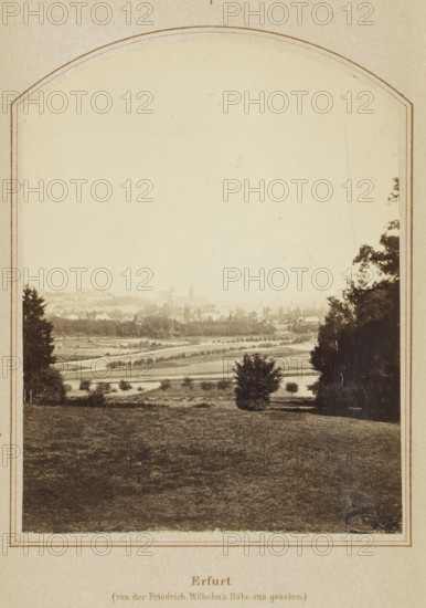 Erfurt in seiner Vergangenheit und Gegenwart, book, publisher: Carl Villaret, Erfurt (city), 1868, Thuringia, textile materials, pasteboard, paper, linen (material), printing, lithography, albumen print, height 185 mm x width 126 mm x thickness 14 mm, Book contains a fold-out map of Erfurt., A sepia-toned photograph framed by an arched border shows a broad grassy foreground leading down to a patchwork of fields and tree-lined paths, with scattered small trees and shrubs across the midground; a distant town with clustered buildings and a few taller spires rises faintly through haze on the horizon, and larger trees border the scene on the left and right edges.
