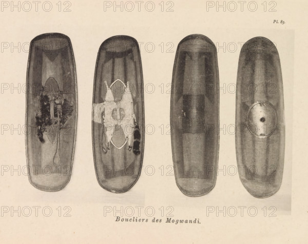 Boucliers des Mogwandi, Four shields of the Ngbandi, page, photomechanical print, number: 'Pl. 83.', photographer: Franz Thonner, cliché maker: Stengel & Markert, Dresden, 1896, Saxony, paper, collotype, photoprint, height 109 mm x width 161 mm, protective weapons: shield, Four elongated oval wooden shield-like objects are arranged horizontally across a pale background, each shown with a top-to-bottom orientation. The leftmost object has a dark textured surface with a central area showing rough, fibrous material and a looped cord hanging downward; the second from left has a similar textured surface with a patched, irregular cloth or hide affixed near its center and edges of frayed material extending from it. The third object from left appears smoother and darker with faint linear striations and a subtle central raised area, while the rightmost object shows concentric fine lines near its top and a round metal or disc-like plate attached off-center toward its lower half. The overall imag...