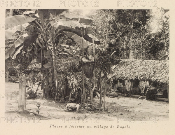 Square with idols in Bogolo (former title), Square with religious images in Bogolo, Places à fétiches au village de Bogolo, page, photomechanical print, number: 'Pl. 60.', photographer: Franz Thonner, Congo (country), cliché maker: Stengel & Markert, Dresden, 1896, Saxony, paper, collotype, photoprint, height 110 mm x width 161 mm, village square, A sepia-toned photograph shows a rustic outdoor scene with large broad-leaf plants and tall stems in the foreground, some leaves appearing torn or drooping. Interwoven wooden poles and bundles of dried leaves form a rough fence or enclosure around a central cluster of vegetation. Thatched structures with overlapping dried foliage create shaded areas, beneath which woven mats and reclining figures can be seen partially obscured. A weathered tree stump stands near the front edge of the scene and a small young plant grows from the ground nearby. In the background dense trees and undergrowth fill the upper portion of the image, and scattered bran...