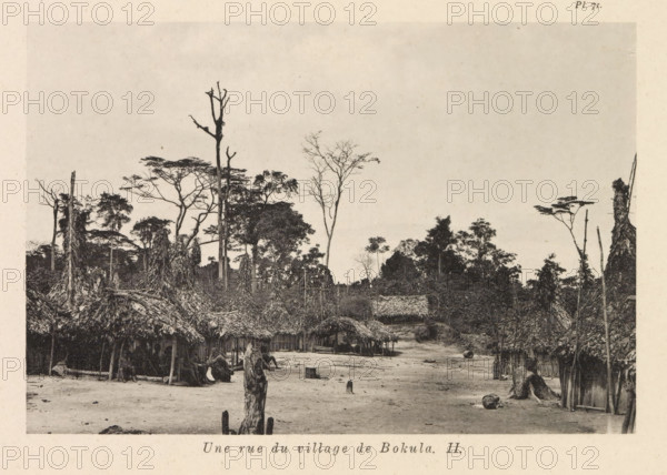 View of a street in Bokula, Une rue du village de Bokula II, page, photomechanical print, number: 'Pl. 71.', photographer: Franz Thonner, Bokula, cliché maker: Stengel & Markert, Dresden, 1896, Saxony, paper, collotype, photoprint, height 108 mm x width 161 mm, street, housing, A wide dirt clearing bordered by clusters of thatched huts with roofs made of layered vegetation and simple wooden supports, some huts arranged along a faint path leading toward a denser treeline; scattered tree stumps and upright wooden posts rise from the ground, and rough logs and cylindrical objects lie on the clearing; in the background thin tall trees with sparse branches and broader canopied trees form a forest edge that fills the upper half of the scene under a pale sky.