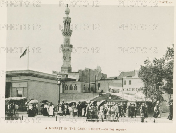 View of a replica of a street from Cairo with a minaret at the World's Columbian Exposition in Chicago in 1893, A minaret in the Cairo street.- on the Midway, page, photomechanical print, number: 'Plate 101', photographer: Charles Dudley Arnold, Chicago, photographer: HD Higinbotham, clichémaker: anonymous, 1893, Charles Dudley Arnold, HD Higinbotham, photographer, clichémaker, North America, Illinois, paper, collotype, photogravure, height 133 mm x width 191 mm, temple, shrine, Islam, Mohammedanism, world fair, world exhibition, World's Columbian Exposition, A city street scene with a tall ornate minaret rising above a row of flat-roofed buildings, a flag flying from a pole on one rooftop, a lamppost in front of a building with arched windows, a canopyed awning extending over part of the sidewalk, a large tree on the right, and many people wearing early twentieth-century clothing and carrying umbrellas or hats gathered and walking in the foreground.